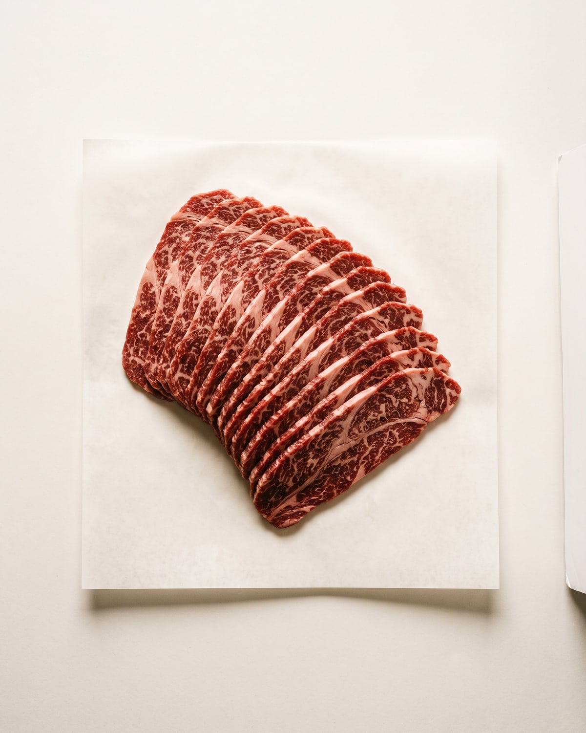 Thinly sliced Iga beef chuck roll fanned out on white paper