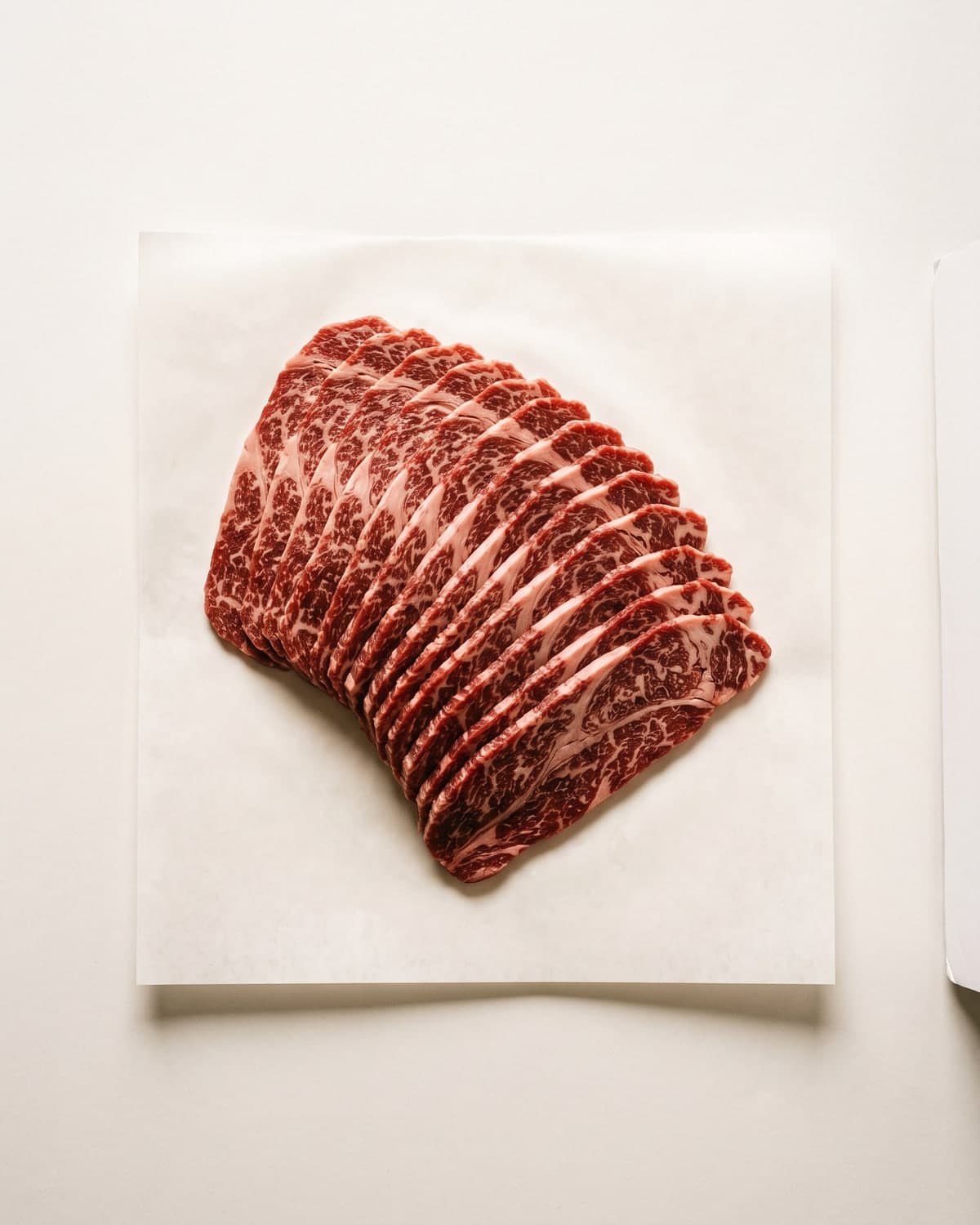 Thinly sliced Iga beef chuck roll fanned out on white paper